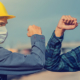 Two workers in construction industry on jobsite wearing masks and bumping elbows due to COVID concerns.