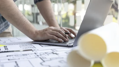 Architect working on computer with blueprints laid out