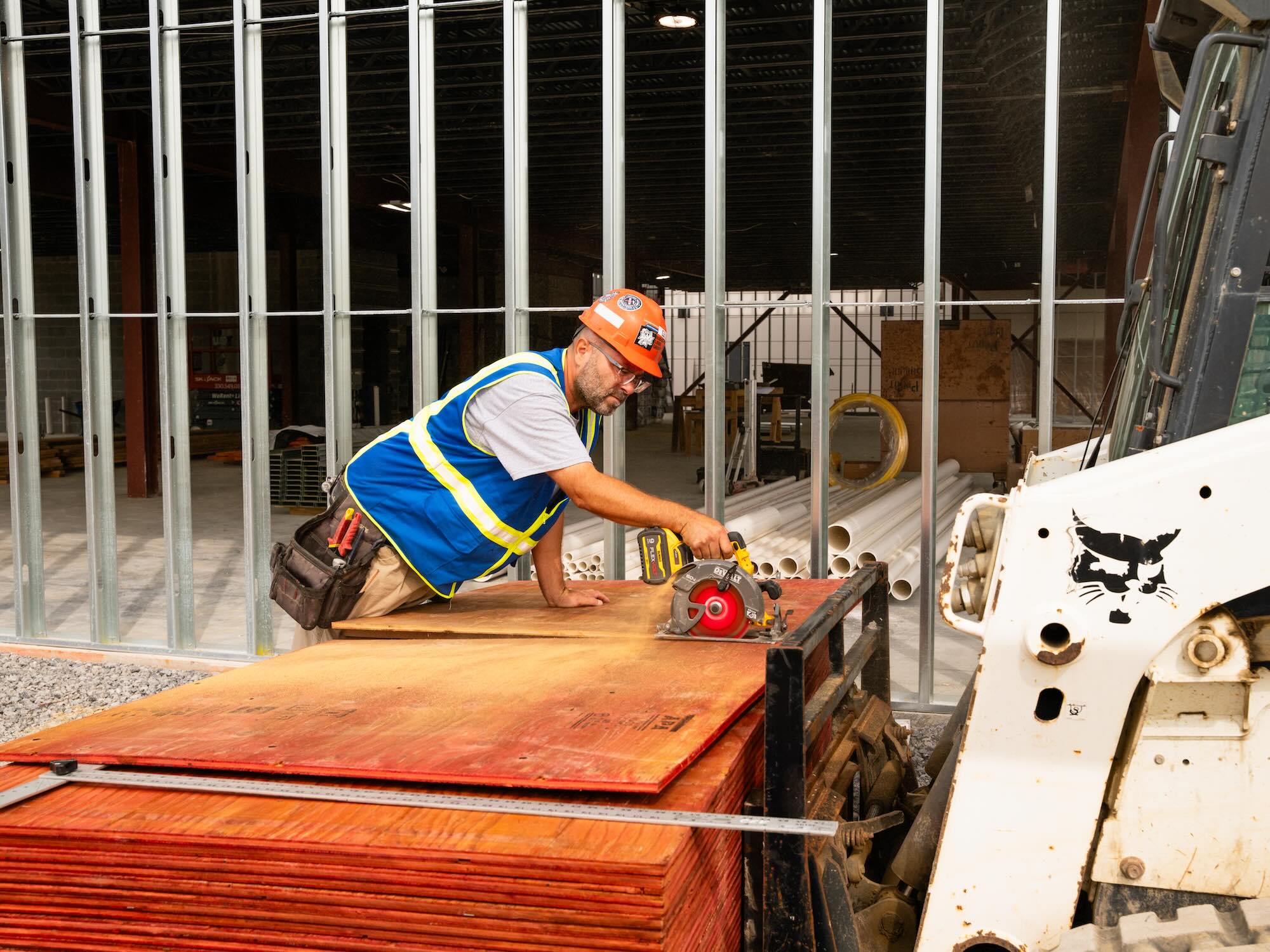 Man wearing safety gear using hand saw on wood sheets outside