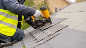 man wearing safety vest using nail gun to nail shingles to commercial roof