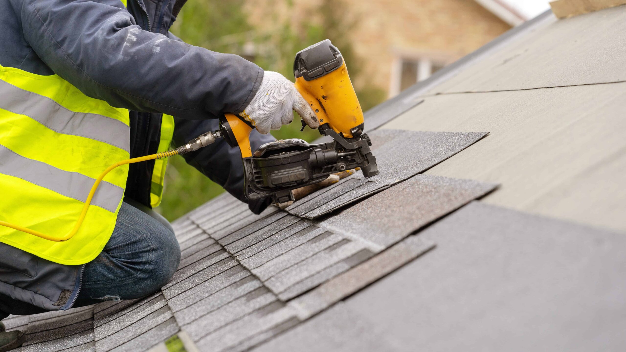 man wearing safety vest using nail gun to nail shingles to commercial roof